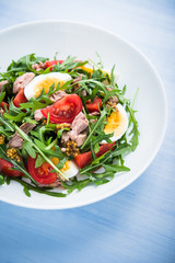 Fresh salad with tuna, tomatoes, eggs, arugula and mustard on blue wooden background close up. Healthy food.