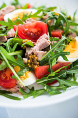 Fresh salad with tuna, tomatoes, eggs, arugula and mustard on blue wooden background close up. Healthy food.