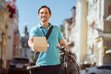 Cheerful professional courier delivering the box