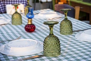Table setting with green glasses and oil lamp on green plaid tablecloth.