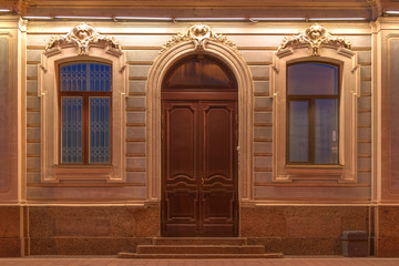 Two windows and door in a row on night illuminated facade of urban apartment building front view, St. Petersburg, Russia.