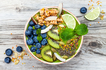 Matcha green tea breakfast superfoods smoothies bowl topped with chia, flax and pumpkin seeds, bee pollen, granola, coconut flakes, kiwi and blueberries. Overhead, top view, flat lay