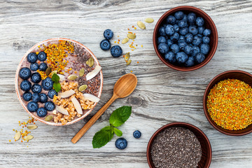 Acai breakfast superfoods smoothies bowl topped with chia, flax and pumpkin seeds, bee pollen, granola, coconut flakes and blueberries. Overhead, top view, flat lay