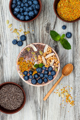 Acai breakfast superfoods smoothies bowl topped with chia, flax and pumpkin seeds, bee pollen, granola, coconut flakes and blueberries. Overhead, top view, flat lay