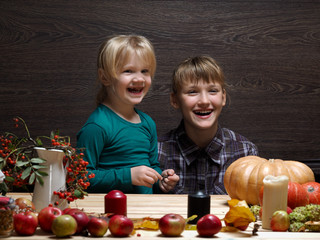 Naklejka premium Children are prepared to meet the autumn holiday Halloween. Two sisters at the table. Pumpkin, rowan tree, decorations for the holiday. Laughter, joy, emotion,