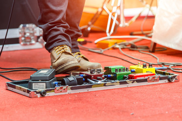 Feet of guitar player on a stage with set of distortion effect pedals. Selective focus