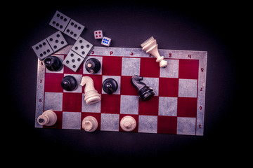 Various board games and figurines over checkers board and dark background. Metaphor for gaming and...