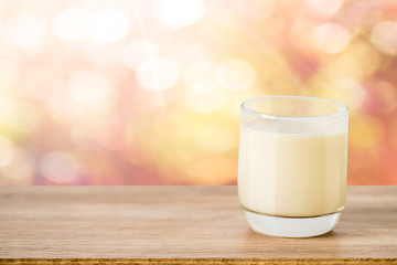 glass of milk on wooden table mock up over blurred garden bokeh in morning sun light background.
