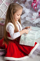 Girl in Christmas dress opens presents.