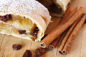 Apple strudel with icing sugar, cinnamon sticks, wooden background
