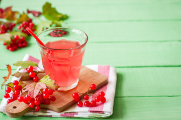 Fresh viburnum drink in glass on green wooden background with leaves and berries. Selective focus.