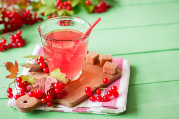 Fresh viburnum drink in glass on green wooden background with leaves and berries. Selective focus.