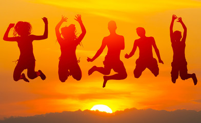 Fototapeta na wymiar Teenage boys and girls jumping high in the air against colorful sunset sky in summer