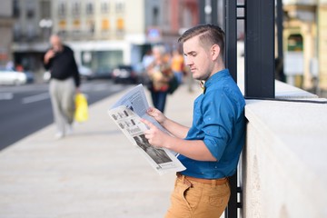 Young man reading the newspaper while waiting in a crowded street