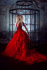 Fashion blonde in red dress with fluffy skirt near the birdcage, concept of liberation
