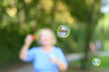 Senior woman blowing iridescent soap bubbles