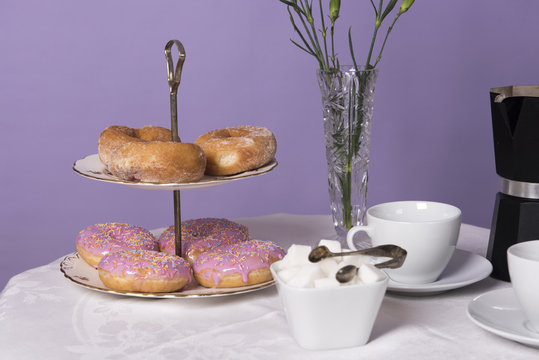 Table set up with coffee, donuts and sugar. Taken on a purple background. 