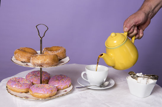 Unrecognisable hand pouring a cup of tea at a table with doughnuts 