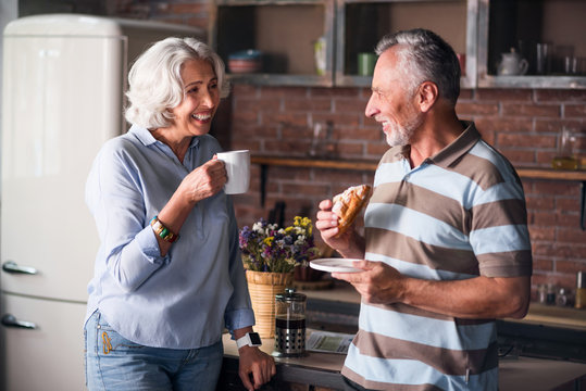 Happy elderly couple smiling at each other while drinking coffee
