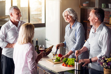 Four nice elderly people gathered around table in kitchen