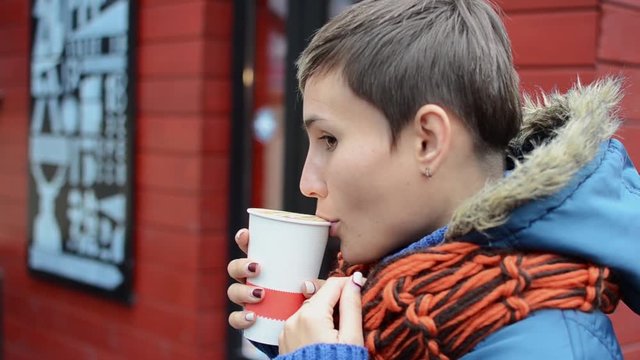 Woman drinks cooffee. Outdoor video. Autumn in the city.