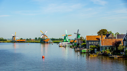 View from the Zaan River of old Dutch Windmills and historic houses along the river at the historic villages of Zaanse Schans and Zaandijk in the Netherlands