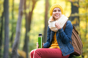 Beautiful woman in autumn forest, thermos and cup