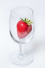Red and ripe strawberry in wineglass on a white background