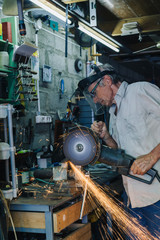 Fototapeta na wymiar Side view of senior workman working with circular grinder in his hands producing flash of sparkles