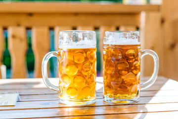 Two mugs of beer on wooden table, sunny day