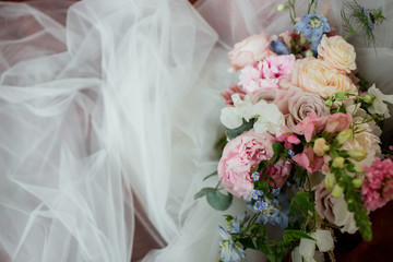 Pastel wedding bouqet made of roses and peonies lie over bride's