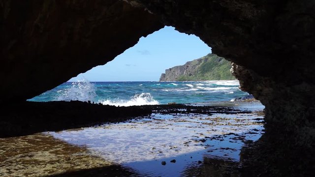 Coastal landscape seen from a hole in the rock with waves breaking on the shore, Rurutu island, south Pacific ocean, Austral archipelago, French Polynesia
