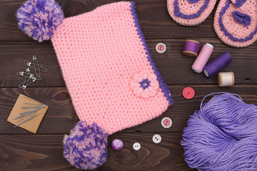 Knitted baby cap and Slippers, yarn for knitting on wooden table. The view from the top. Sewing accessories.