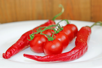cherry tomatoes and pods of chili peppers on plate