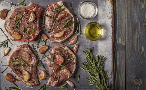 Raw pork chops with spices on a metal baking sheet.