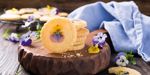Homemade shortbread cookies with edible flowers on old wooden background. Holiday food