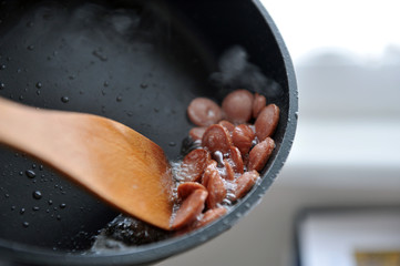 Vegetable soup with added pieces of frankfurter sausages in a white plate.