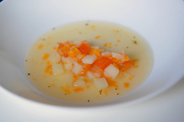 Vegetable soup with added pieces of frankfurter sausages in a white plate.