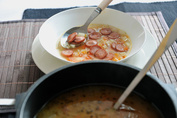Vegetable soup with added pieces of frankfurter sausages in a white plate.