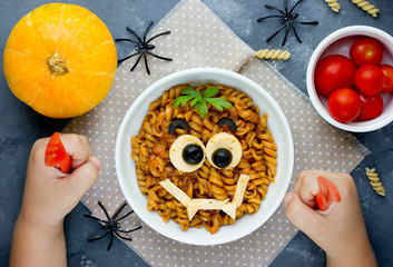 Child eat pasta with sauce in the shape of a smiling vampire face