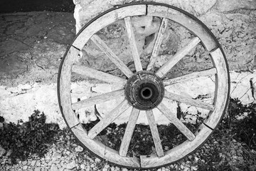Fototapeta na wymiar Old wooden wheel stands near rural wall