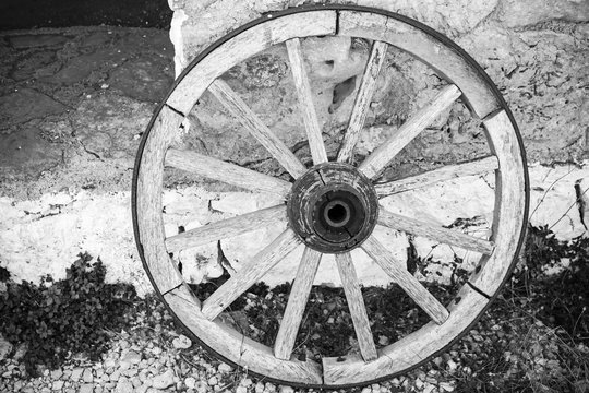 Old wooden wheel stands near rural wall