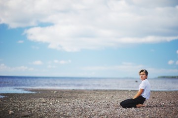 Naklejka na ściany i meble young girl in white blouse and black trousers yoga by the sea on the background of beautiful clouds in the blue sky.