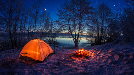 Illuminated tent in the winter camp by the lake at night with stars