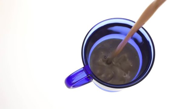 Top view of a serving of fat free coffee milk being poured into a blue mug on a white background.