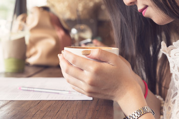 Young asian woman holding coffee cup in hand with pen and paper on table