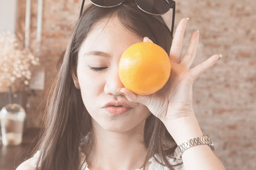 Young asian woman closing eyes and holding orange in hand, soft vintage
