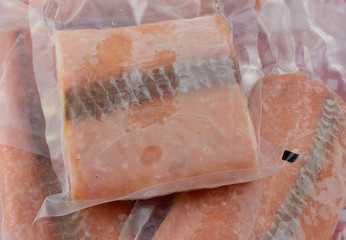Frozen salmon fillets in vacuum plastic packaging covered with frost as taken out to thaw