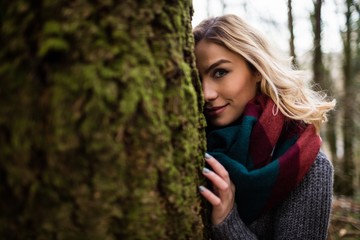 Beautiful woman hiding behind tree trunk in forest