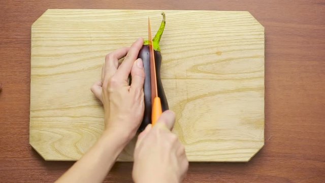 Hands of woman cutting eggplant on wooden board. view from above